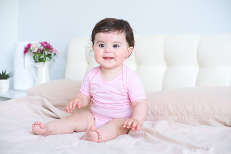 portrait of smiling healthy baby in pink bodysuit on bedの写真素材