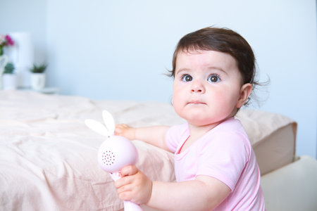 cute smiling baby with plastic bunny toy standing holding on to the bed frameの写真素材