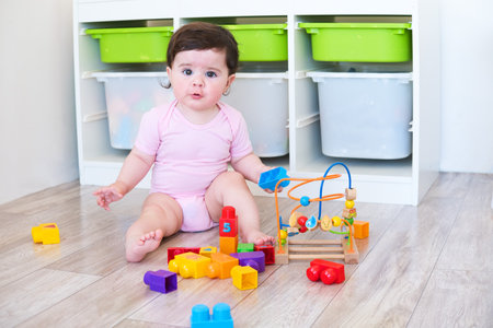 funny baby girl in pink bodysuit playing with colorful toys on floorの写真素材