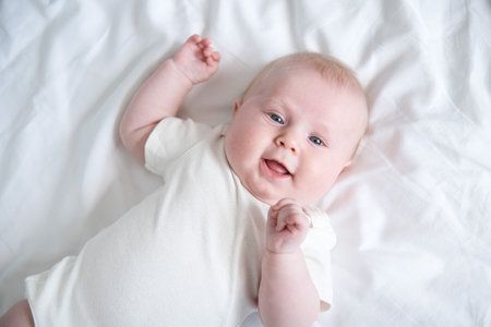 healthy smiling baby lies on his back on bed on white bedding. top viewの写真素材