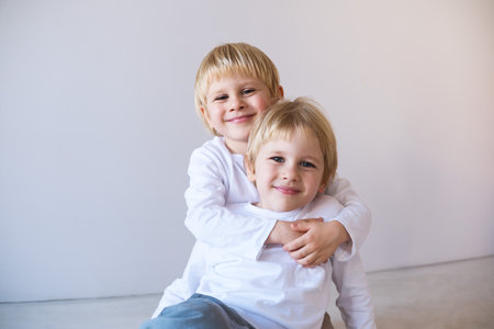 two little blonde smiling boys twins hugging, sitting on floor.の写真素材