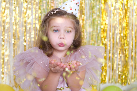 happy child girl with long hair in pink dress blowing confetti and celebrating her birthday.の写真素材