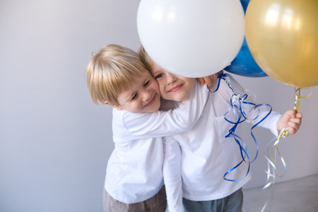 two little blonde smiling boys twins hugging, holding balloons celebration birthdayの写真素材