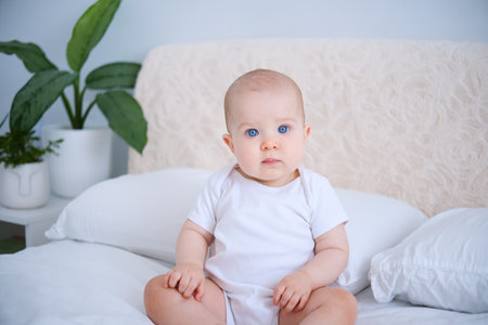 portrait of smiling healthy baby in white bodysuit sitting on bed. copy spaceの写真素材