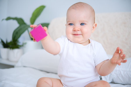 funny baby girl in white bodysuit playing with wooden toy on bed