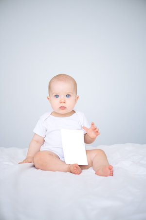 portrait of smiling healthy baby in white bodysuit on bed with mock up cardの写真素材