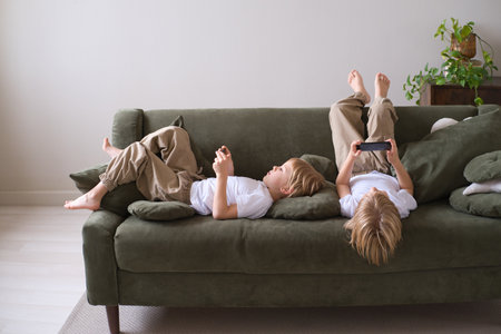 kids boys twins using smartphones lying on the couchの写真素材