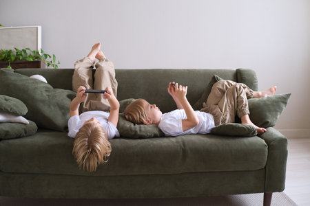 kids boys twins using smartphones lying on the couchの写真素材