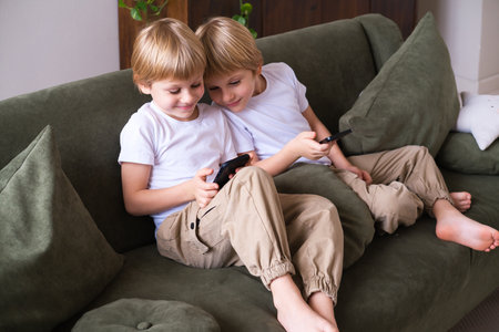 kids blonde boys twins using smartphones on the couch in living roomの写真素材