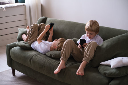 kids boys twins using smartphones lying on the couchの写真素材