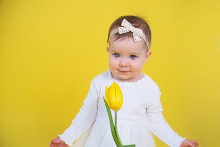 Cheerful happy child with tulip flower. little girl in white dress on yellow background.の写真素材