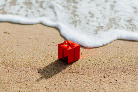 present gift in red box  on the beach in tropics. Present red box flowing in the sea. christmas holideys on the beachの写真素材