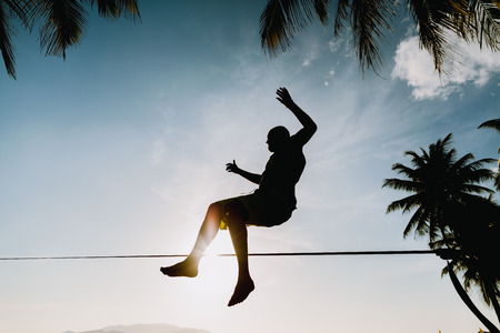 teenage  jumping and balancing on slackline silhouette and sunflareの写真素材