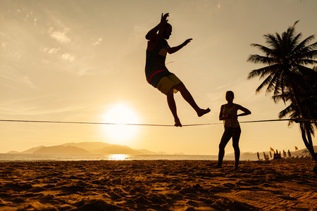 teenagers balance slackline on sunrise beach silhouetteの写真素材