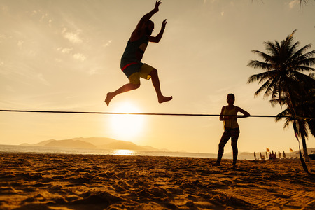 teenagers balance slackline on sunrise beach silhouetteの写真素材