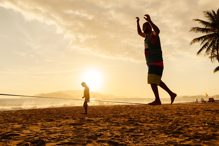 teenagers balance slackline on sunrise beach silhouetteの写真素材