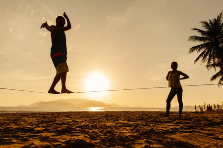 teenagers balance slackline on sunrise beach silhouetteの写真素材