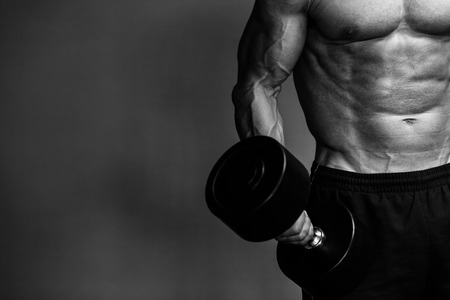 Close up of muscular bodybuilder guy doing exercises with weights over grey background. Black and whiteの写真素材