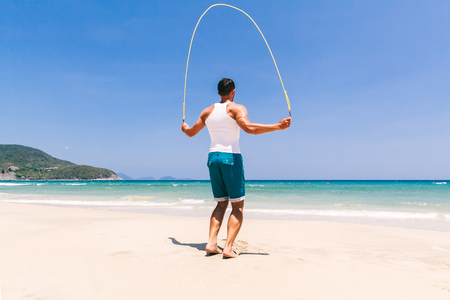 fitness man skipping on the beach with rope near the ocean with blue skyの写真素材
