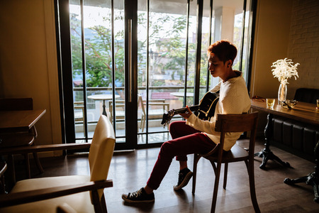 asian handsome guitarist artist man play acoustic guitar in cafe. Shot through the windowの写真素材