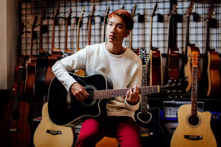 handsome asian teenage man playing acoustic guitar in guitar shopの写真素材