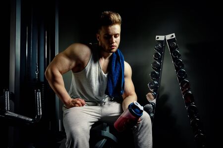 strong bodybuilder athlete with protein shaker and towel tired of work out with dumbbellsの写真素材
