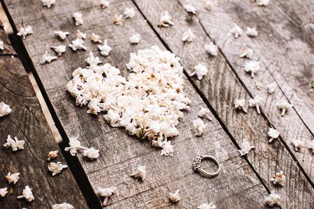 gentle beautiful white heart shape lilac flowers with proposal wedding ring on vintage wood tableの写真素材