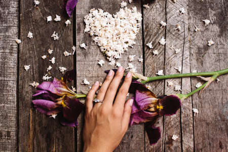 heart shape white lilac flowers and violet irises with on hand proposal wedding ring on vintage wood tableの写真素材