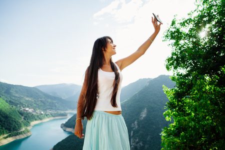 happy girl taking selfie photo on telephone phablet with picturesque landscape mountains in Montenegroの写真素材