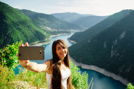 happy girl taking selfie photo on telephone phablet with picturesque landscape mountains in Montenegroの写真素材