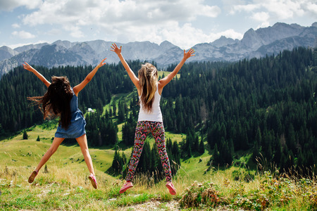 two long hair girls happy jump in mountains with exciting view of Montenegro, back viewの写真素材
