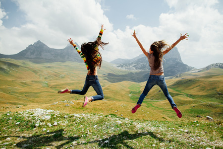 two long hair girls happy jump in mountains with exciting view of Montenegro, Durmitor, back view