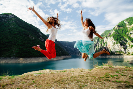 two long hair girls happy jump in mountains with exciting view of Montenegroの写真素材