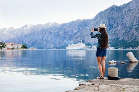 girl taking photo on smartphone of cruise liner yacht in picturesque landscape bay water bakground viewの写真素材