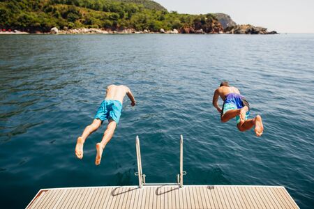 men jumping into sea water from yacht party vacationの写真素材
