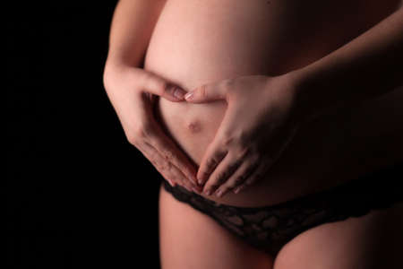 Closeup of pregnant woman make hands heart shape on the tummy.の写真素材