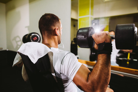 handsome bodybuilder pumping hands with dumbbells in gymの写真素材