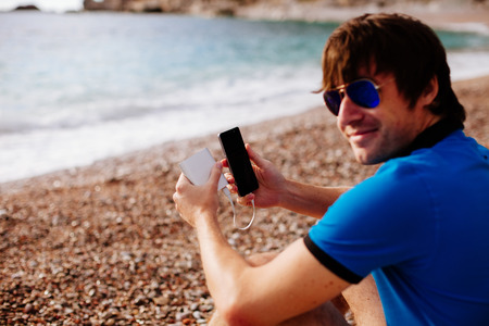 man charging smartphone with powerbank on vacations at sea sideの写真素材