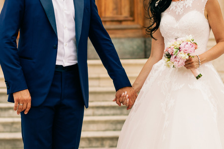 bride and groom hold hands together with wedding bouquet. Hands close up shotの写真素材
