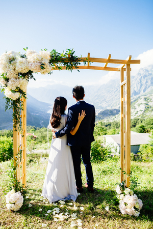 honeymoon wedding couple travel back view. Wedding arch,  mountains and sea background in Montenegro. Fine art wedding styleの写真素材