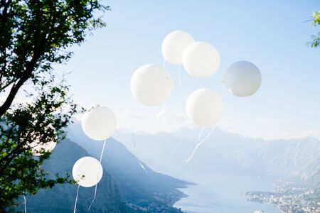 white ballons fly at blue sky. Mountains and sea view backgroundの写真素材