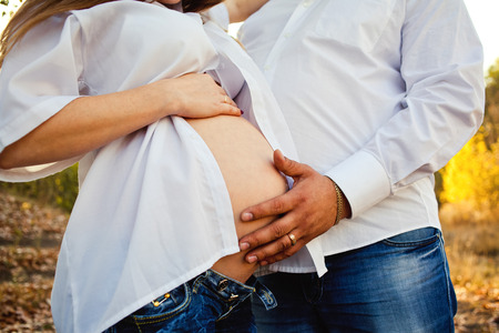 Pregnant woman and man relax outdoors. Pregnant couple in autumn foresの写真素材