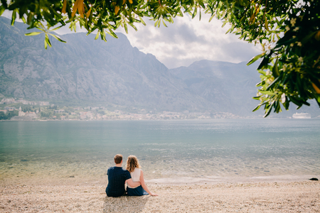 lovely couple relax on beach together. Mountains and Kotor Bay view with cruise ship behindの写真素材