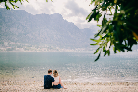 lovely couple relax on beach together. Mountains and Kotor Bay view with cruise ship behindの写真素材