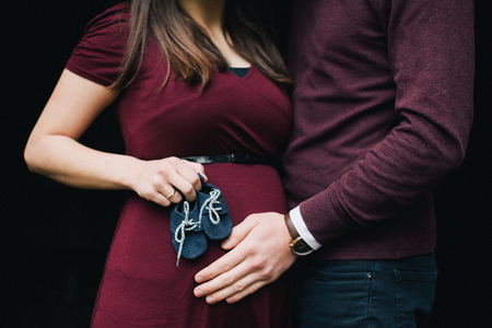 Pregnant woman holding baby booties. Belly with booties close up