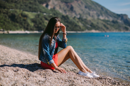 woman sitting on the beach. long hair woman on beach in sunglassesの写真素材
