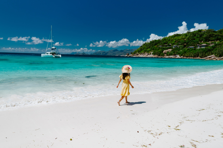 woman relax on tropical beach resort. Fashion sexy woman in summer dress and hat walking on beach of Seychelles.の写真素材