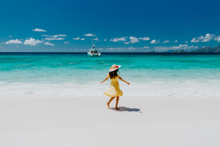 woman travel tropical beach resort with yacht view. Fashion sexy woman in sarong and hat walking on beach of Seychelles.の写真素材