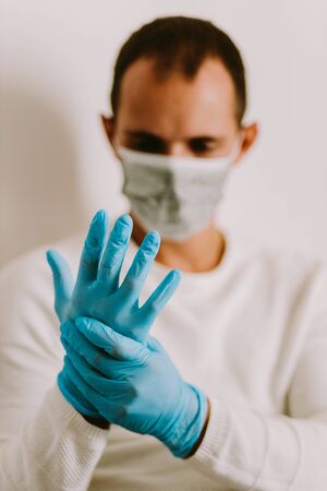 man using latex gloves at home for virus prevention. Male wearing medical gloves and face mask for virus prevention during self isolation on quarantine.の写真素材