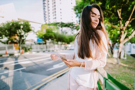 Long hair woman using phone standing outdoors near road. Joyful woman using phone outdoors street.の写真素材